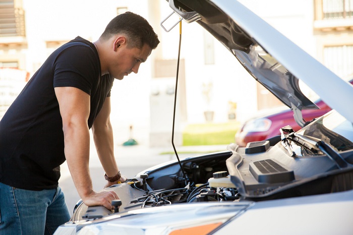 Profile view of a handsome young Hispanic man looking at a car with its hood open, trying to fix it