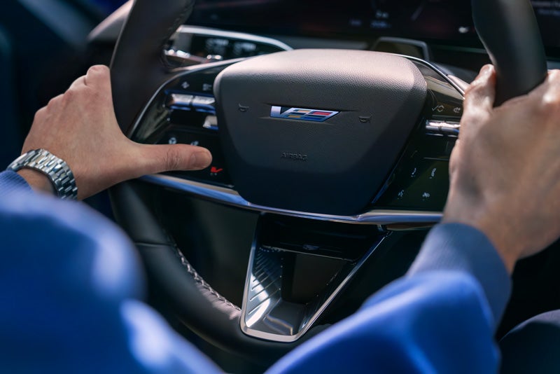 Close-up of a Man About to Press the V-Button on the 2026 OPTIQ-V Steering Wheel | Wilkinson Cadillac in Sanford NC
